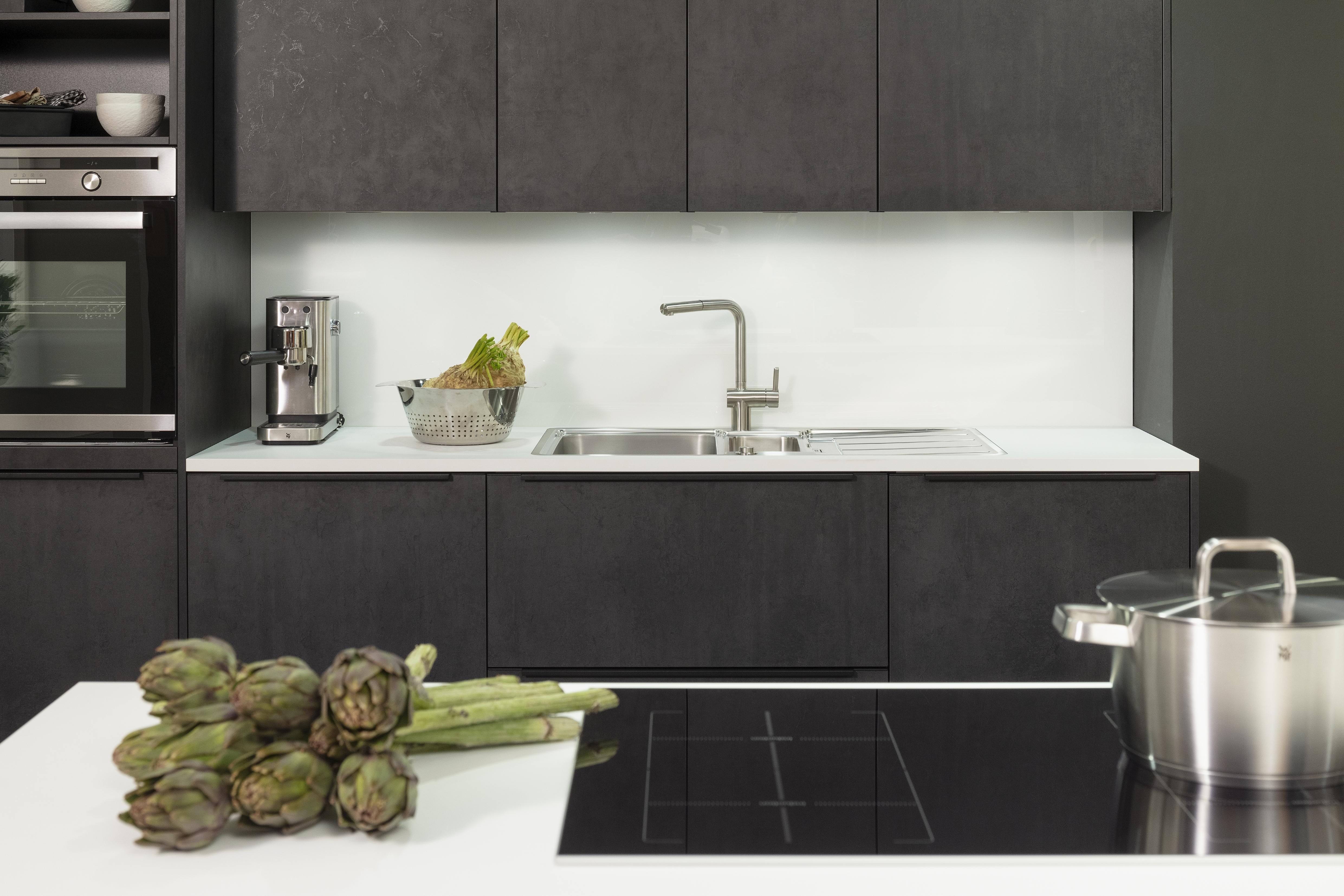 Küchenzeile in Beton-Dekor mit Spüle sowie integriertes Kochfeld im Vordergrund. 