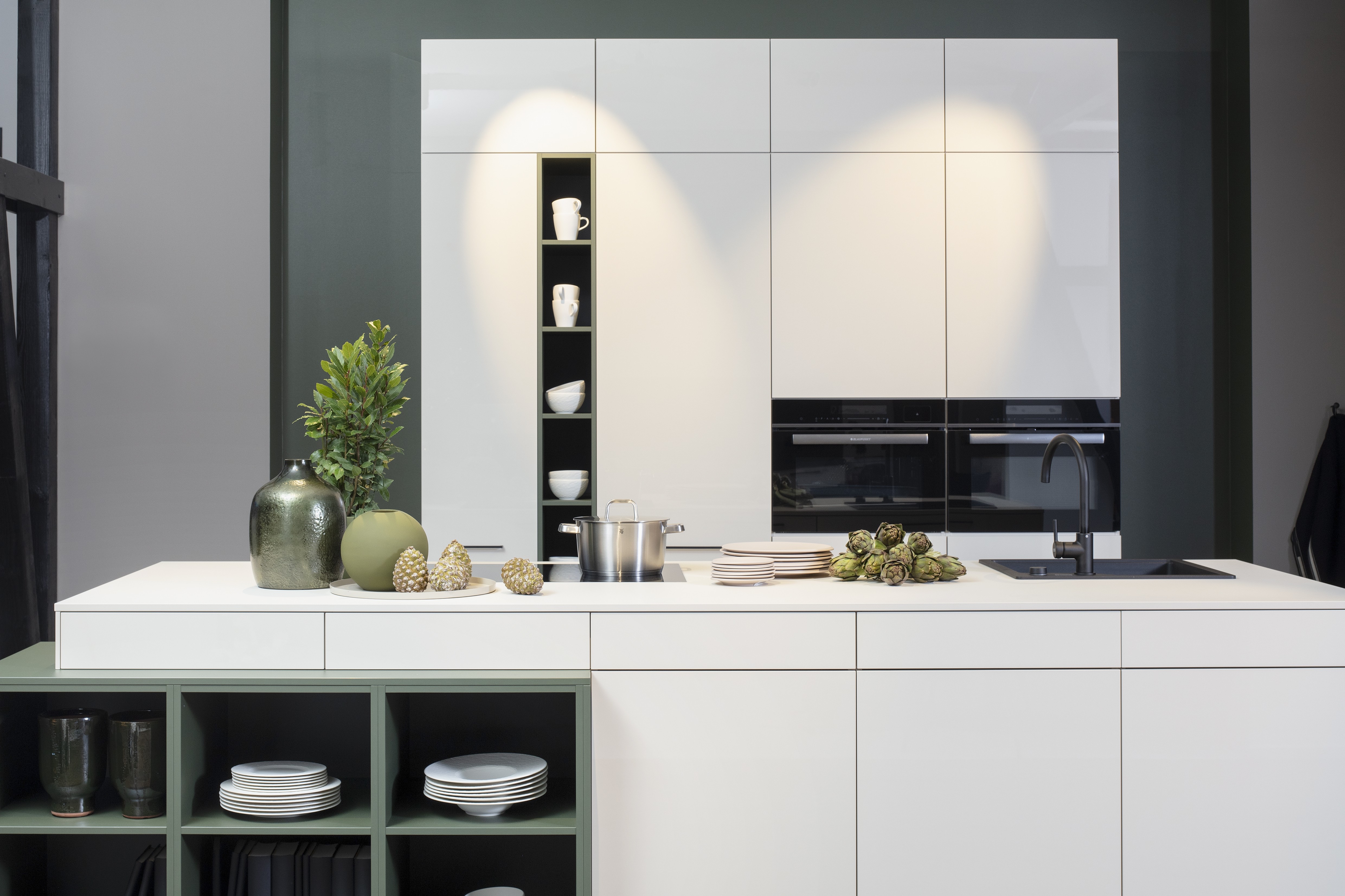 Concept130 Front: Perfect Sense Perfect Brillant Crema magnolia UV Hochglanz lackiert Front 2: Perfect Sense Scala Olivgrün Grüne Front? APL: Perfect Sense Crema Magnolia 16 mm Griff: Schwarz Metall matt Geräte: Blaupunkt Spüle und Armatur: Franke  Features: offene Regale in zweiter Frontfarbe abgesetzt, Apothekerschrank, Spüle in Schwarz.